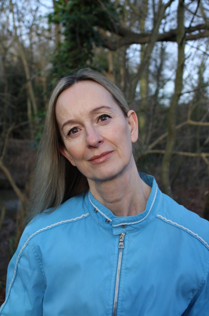 Lisa Kelly wears a blue zip up top against a background of tree branches. 